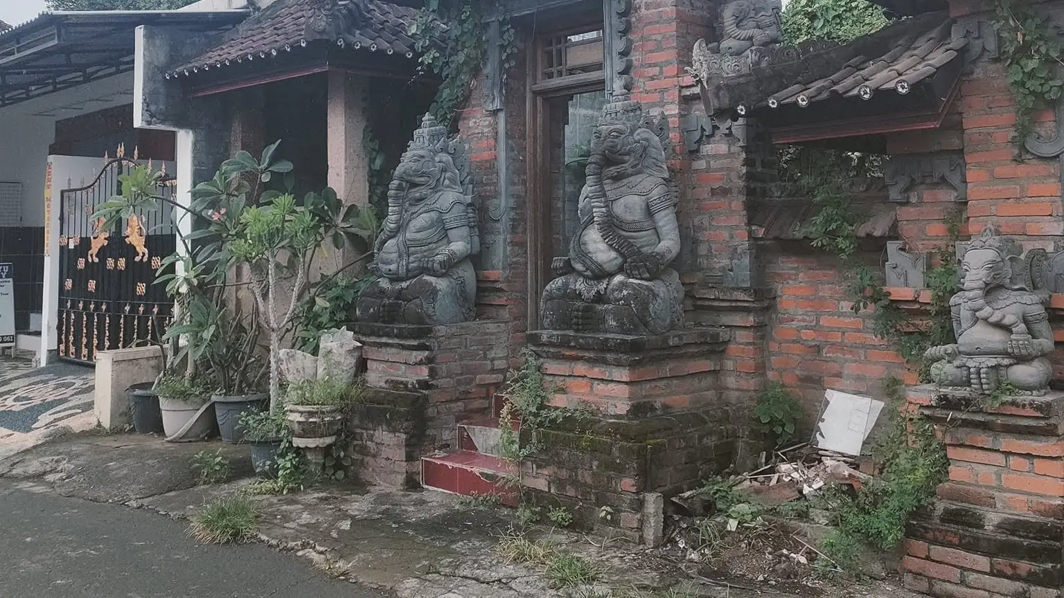 Paved village lane in central Lovina beside a traditional Balinese gate with stone guardian statues